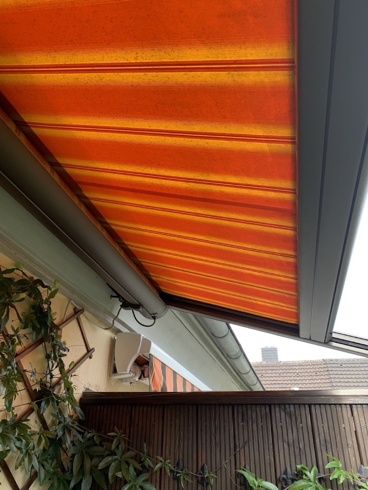 Markise mit orangen Streifen unter einem Dachüberstand