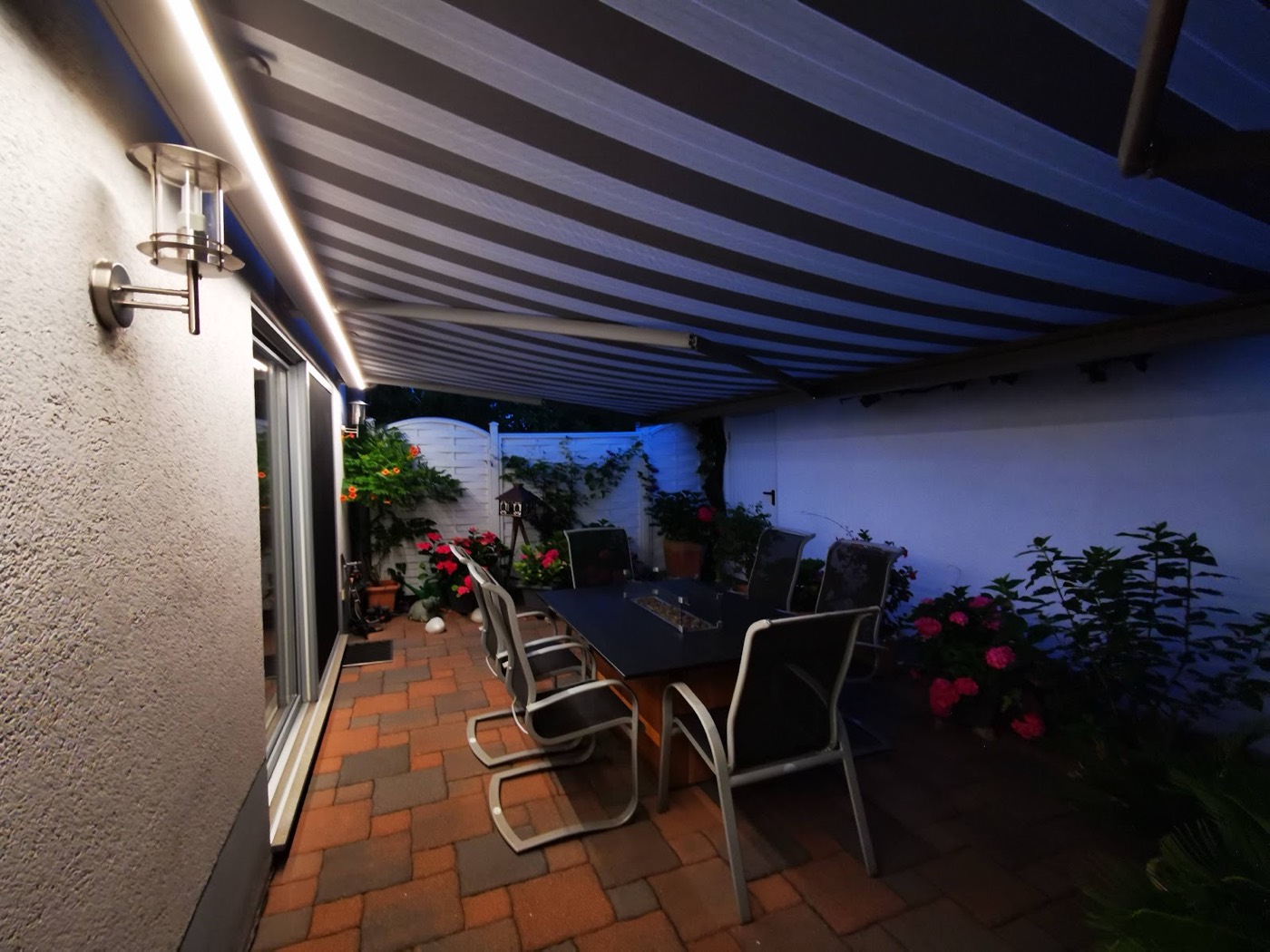 Gestreifte Markise über einer Terrasse am Abend, Lichtleiste an der Hauswand