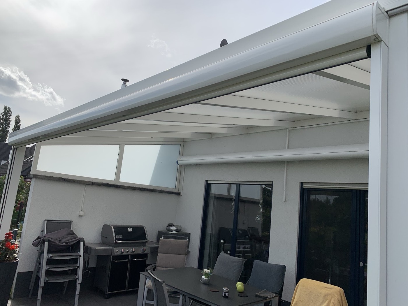 Weißes Terrassendach mit Beschattung, darunter Tisch und Grill